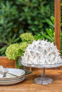 a white cake sitting on top of a wooden table next to plates and silverware