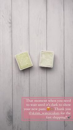 two small square white tiles sitting on top of a wooden floor next to each other