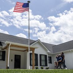 two people riding bikes in front of a house with an american flag