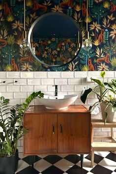 a bathroom sink sitting under a mirror next to potted plants and a wall mounted mirror