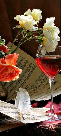 a glass of wine sitting on top of a table next to music sheets and flowers