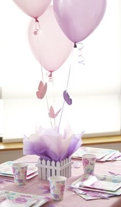 the table is set with pink and purple balloons, paper napkins, and cupcakes