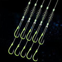 six fishing hooks hanging from the side of a black background with green and white lights