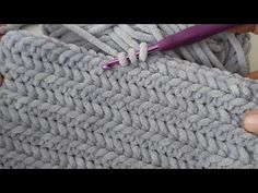 someone is crocheting the edge of a gray blanket with a purple yarn brush