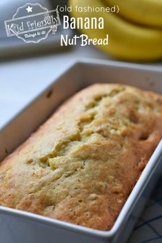 a loaf of banana nut bread in a pan on a table with bananas behind it