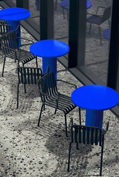 several blue tables and chairs are lined up on the sidewalk outside an office building with glass doors