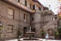 a woman standing in front of an old building next to a fountain with flowers on it