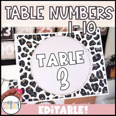 a hand holding up a table number sign with leopard print and black letters on it