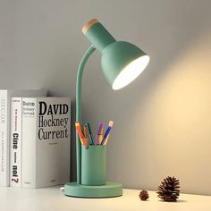 a green desk lamp sitting on top of a table next to a pile of books