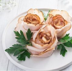 four pieces of meat with parsley on a white plate next to flowers and leaves