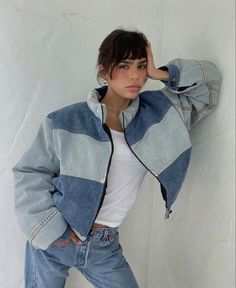 a woman leaning against a white wall with her hand on her head, wearing jeans and a jacket