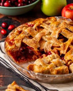 a pie sitting on top of a wooden table next to apples and cranberries