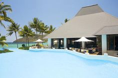 an outdoor swimming pool with tables and umbrellas next to the ocean in front of palm trees