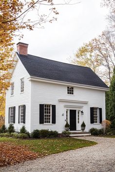 a white house with black shutters on the front and side windows in fall foliage