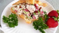 a sandwich with chicken salad and strawberries on a paper plate next to some parsley