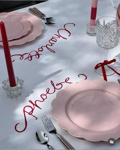 the table is set with pink plates, silverware and red candles for a special occasion