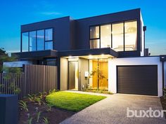 a modern house is lit up at night with the lights on and grass in front