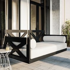 a black and white swing bed on a porch next to a table with a glass vase