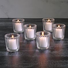 six white candles sitting on top of a wooden table