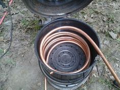 an open metal pot sitting on top of a grass covered ground next to a hose