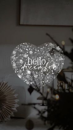 a white heart with the words hello december written on it in front of a christmas tree