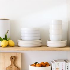 bowls and plates are stacked on a shelf next to books, lemons, and a cutting board