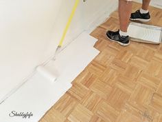 a man is painting the wall with white paint and a yellow tape as he stands next to a pair of shoes