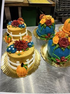 three decorated cakes sitting on top of metal trays