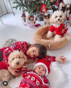 two children and a dog laying on the floor next to a christmas tree with decorations