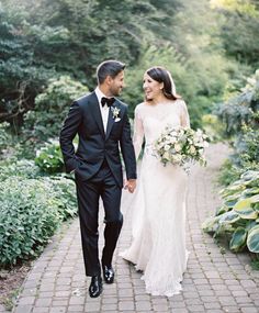 a bride and groom walking down a brick path in their wedding attire, holding hands