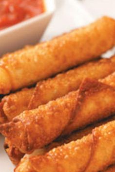 some fried food on a white plate next to a small bowl of sauce and dipping sauce