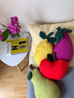 three stuffed fruits and vegetables sit on a pillow next to a table with a book