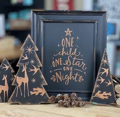 three wooden christmas trees with gold foil on them and a black framed sign that says one child, one star, one night