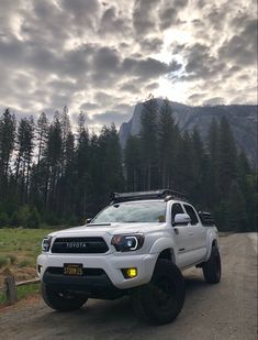 a white truck parked on the side of a dirt road in front of some trees