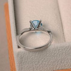 an engagement ring with a blue topazte sits in a white velvet box on display