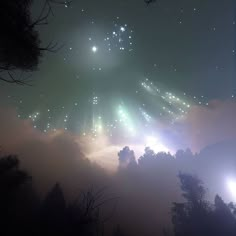 fireworks are lit up in the night sky above some trees and foggy hills with low lying clouds