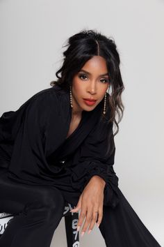 a woman in black is posing for the camera with her hands on her knees and legs crossed