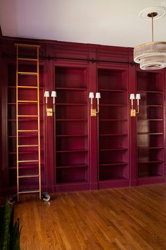 an empty room with red bookcases and a ladder hanging from the ceiling in front of it