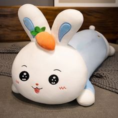 a white stuffed rabbit laying on top of a bed next to a pillow with a carrot on it's head