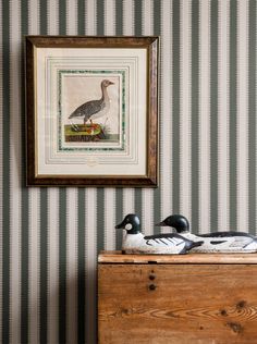 a duck sitting on top of a wooden chest in front of a striped wallpaper