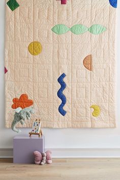 a quilted wall hanging on the side of a white wall next to stuffed animals