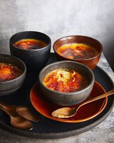 three bowls of soup on a plate with spoons