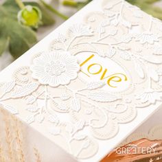 a white box with the word love written in gold on it next to some flowers