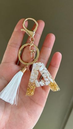 a hand holding a gold key chain with white beads and tassels