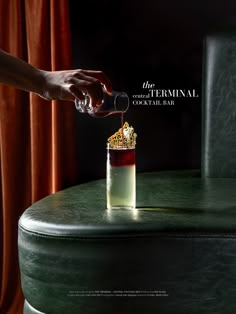 a person pouring something into a glass on top of a green table next to a window