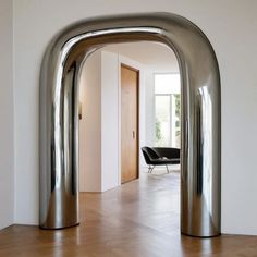 an arch shaped metal object in the middle of a room with wood flooring and white walls