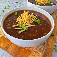 two bowls of chili cheese soup on a cutting board with green onions and parmesan cheese