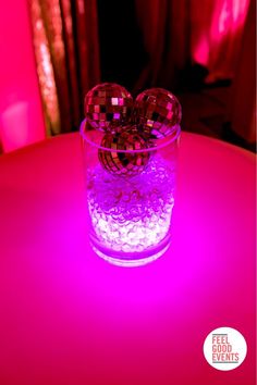 a glass filled with water sitting on top of a pink table next to a window