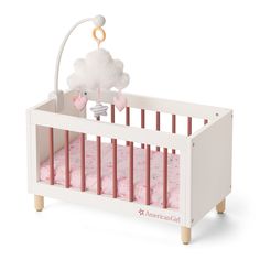 a white crib with pink bedding and clouds hanging from the top of it