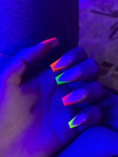 a woman's hand with neon colored nails holding onto her wrist, in front of a purple background